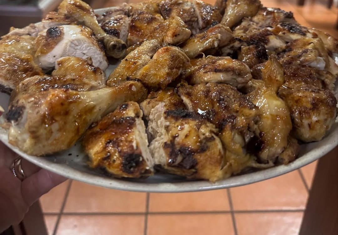 Travessa com frango assado cortado em pedaços, sobre o chão de tijoleira da sala